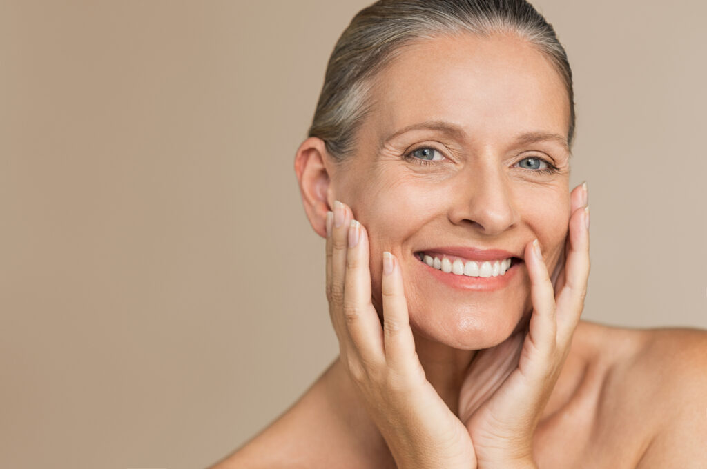 Beauty portrait of mature woman smiling with hand on face. Closeup face of happy senior woman feeling fresh after anti-aging treatment. Smiling beauty looking at camera while touching her perfect skin.